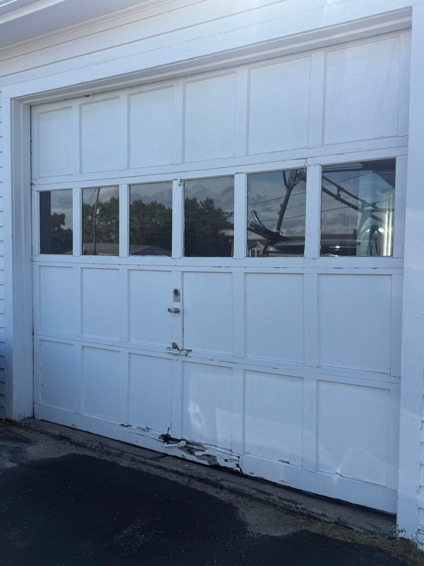 Aging white wooden garage door with damaged bottom panel before replacement
